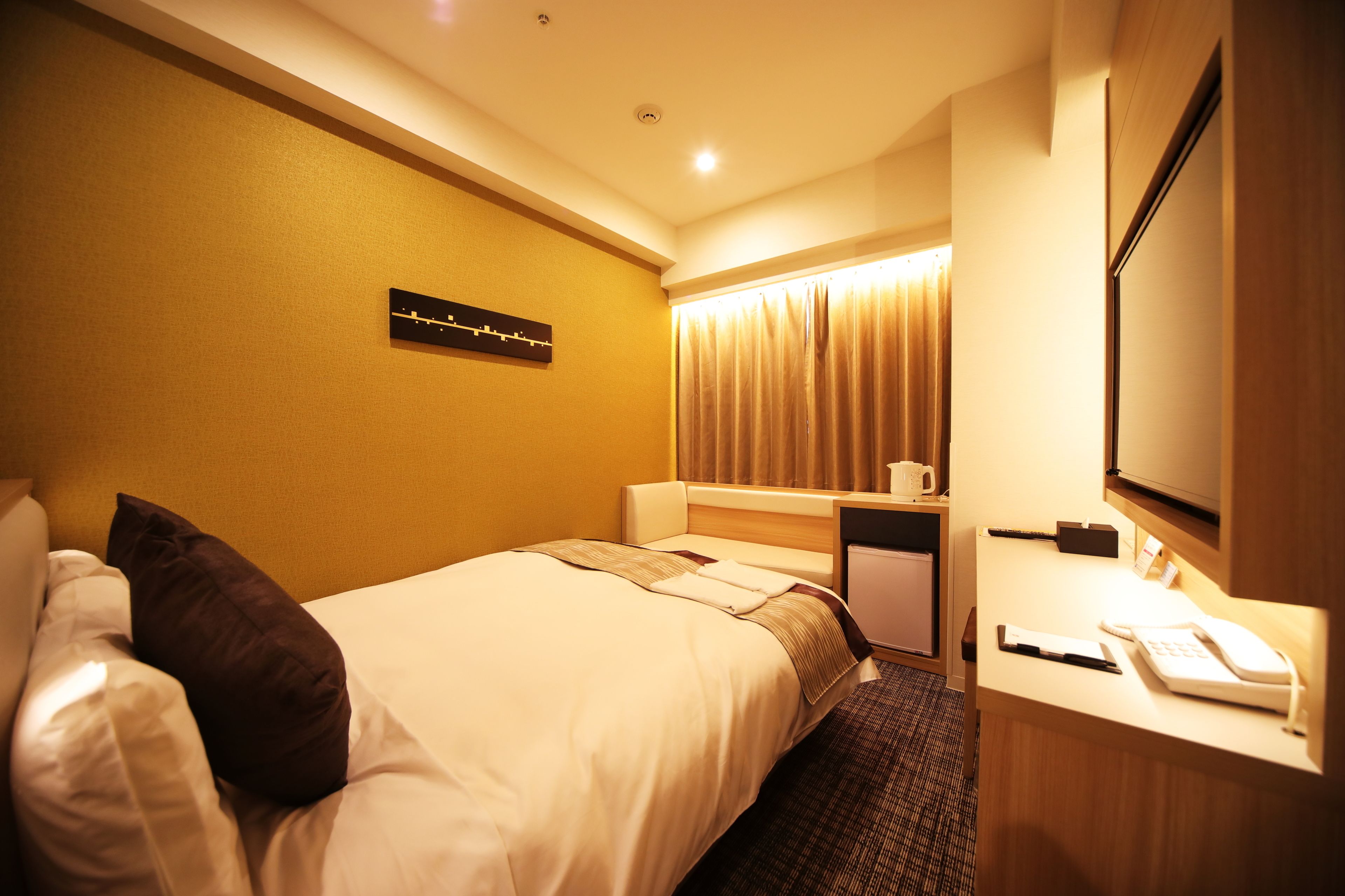 Une chambre d’hôtel avec un lit, un bureau avec un téléphone, un miroir et une horloge au mur.