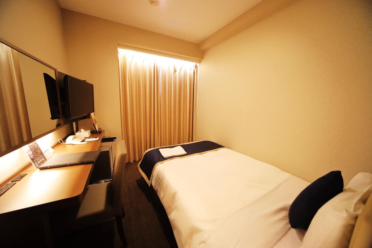 A hotel room with a desk, a bed, a TV, and a window with curtains.