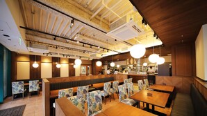 A restaurant with wooden tables and patterned chairs, a bar area, and a high ceiling with exposed beams and lighting fixtures. - Hotel Sunroute Asakusa (Tokyo)
