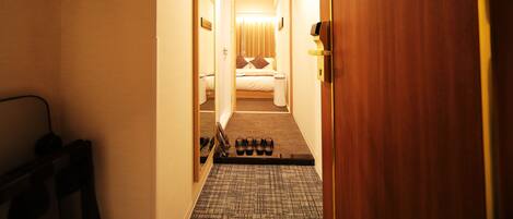 Un pasillo de hotel que conduce a un dormitorio con una cama, una mesita de noche y un espejo.