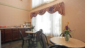A dining area with a round table, striped chairs, a vase with flowers, and a kitchen area with cabinets and a coffee machine. - Americas Best Value Inn Anderson, SC (Anderson)