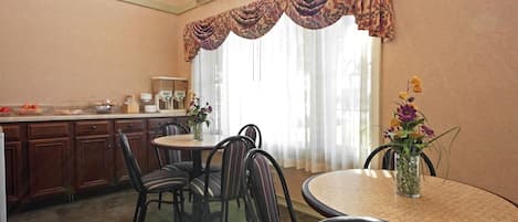 Un comedor con una mesa redonda, sillas a rayas, un florero con flores y una zona de cocina con armarios y una cafetera.