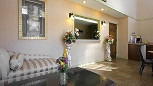 A living room with a sofa, a coffee table, and two vases with flowers. There is a mirror above the sofa and a kitchen area in the background. - Americas Best Value Inn Anderson, SC (Anderson)
