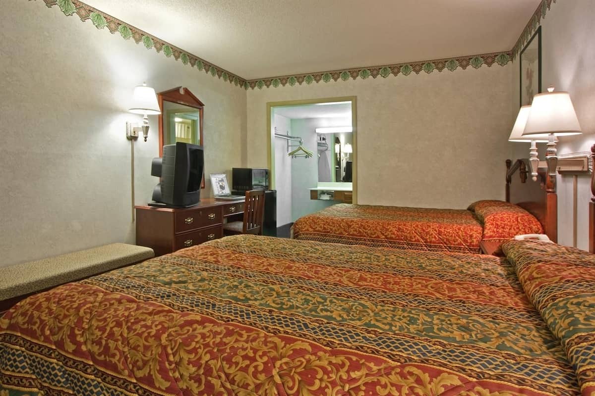 A hotel room with two beds, a desk with a computer, a television, and a mirror.