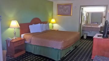 A hotel room with a bed, two bedside lamps, a nightstand, a dresser, a mirror, and a bathroom visible through an open door.