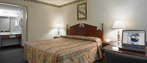 A hotel room with a bed, a desk with a lamp, a chair, a desk lamp, and a framed picture on the wall.