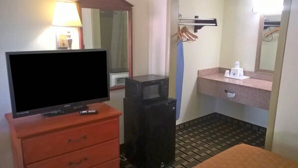 A hotel room with a television on a dresser, a small trash bin, a sink with a mirror, and a towel on the floor.