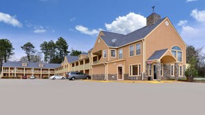 A motel with a central building and two smaller wings, featuring a stone facade, multiple balconies, and a parking lot. - Americas Best Value Inn Anderson, SC (Anderson)
