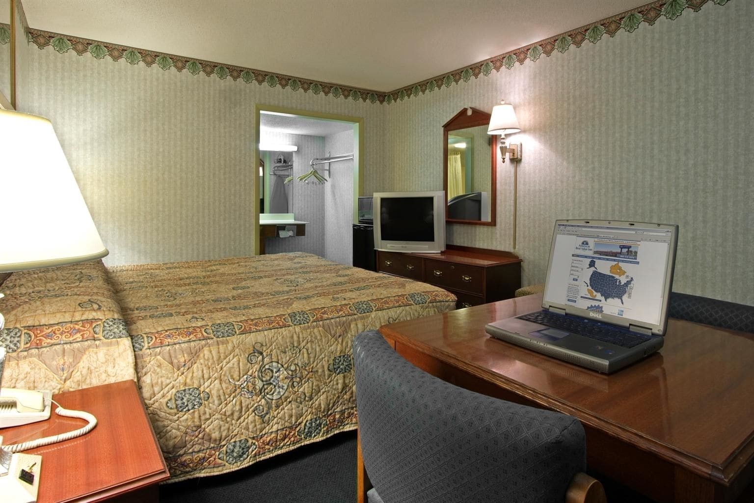 Una habitación de hotel con una cama, un escritorio con una computadora portátil, un teléfono y un televisor.
