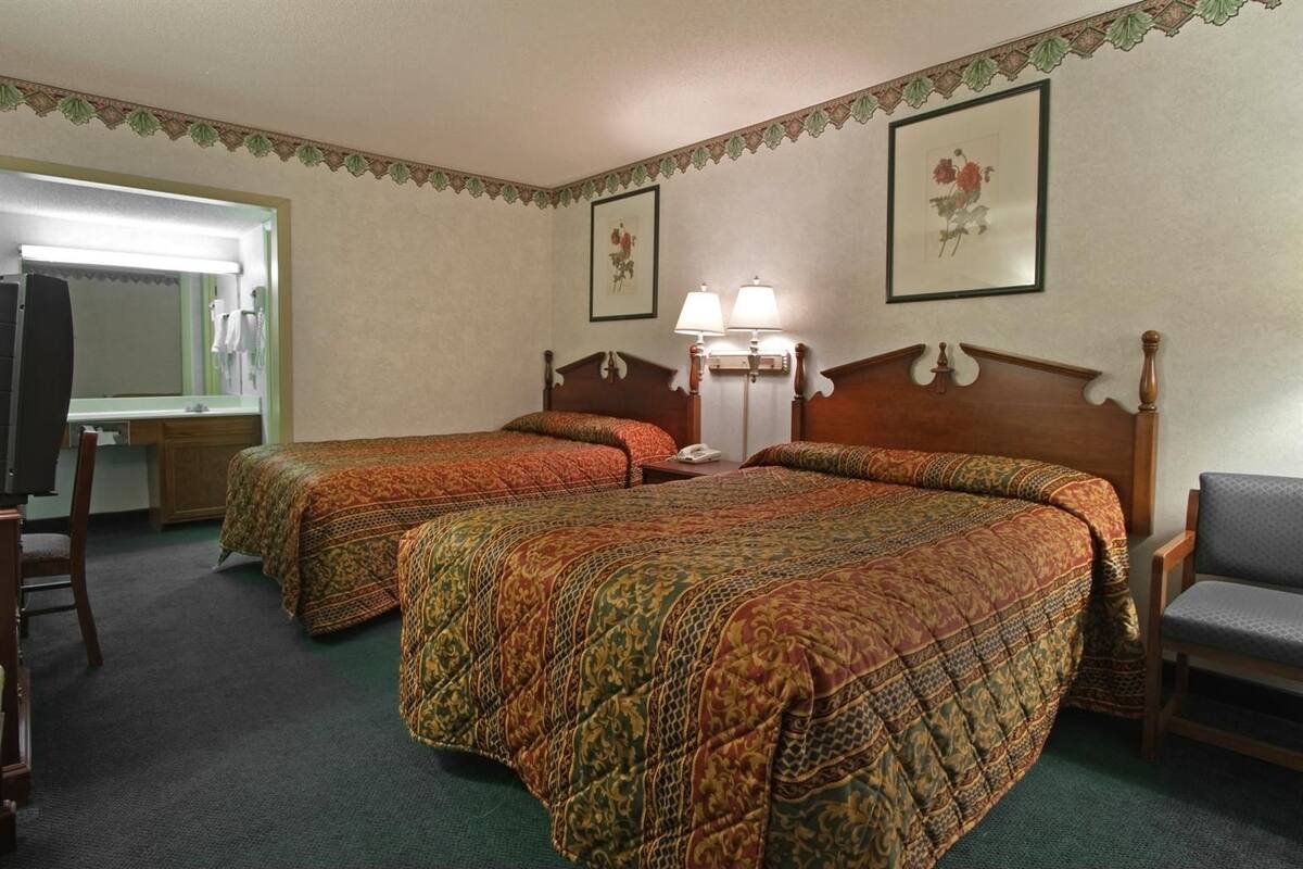 A hotel room with two beds, a desk, a chair, and a mirror.