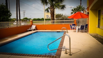A swimming pool with a metal ladder, lounge chairs, and a red umbrella.
