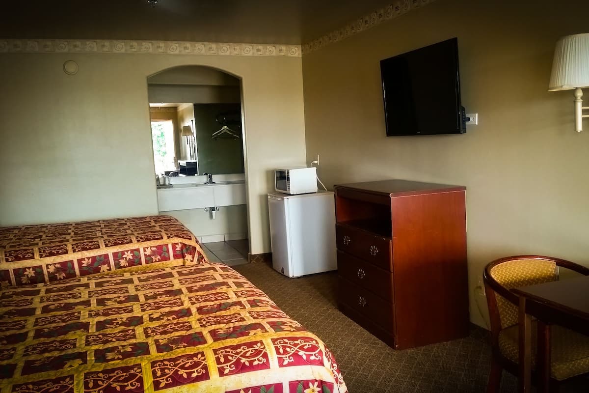 A hotel room with two beds, a desk, a mirror, a TV, a refrigerator, and a lamp.