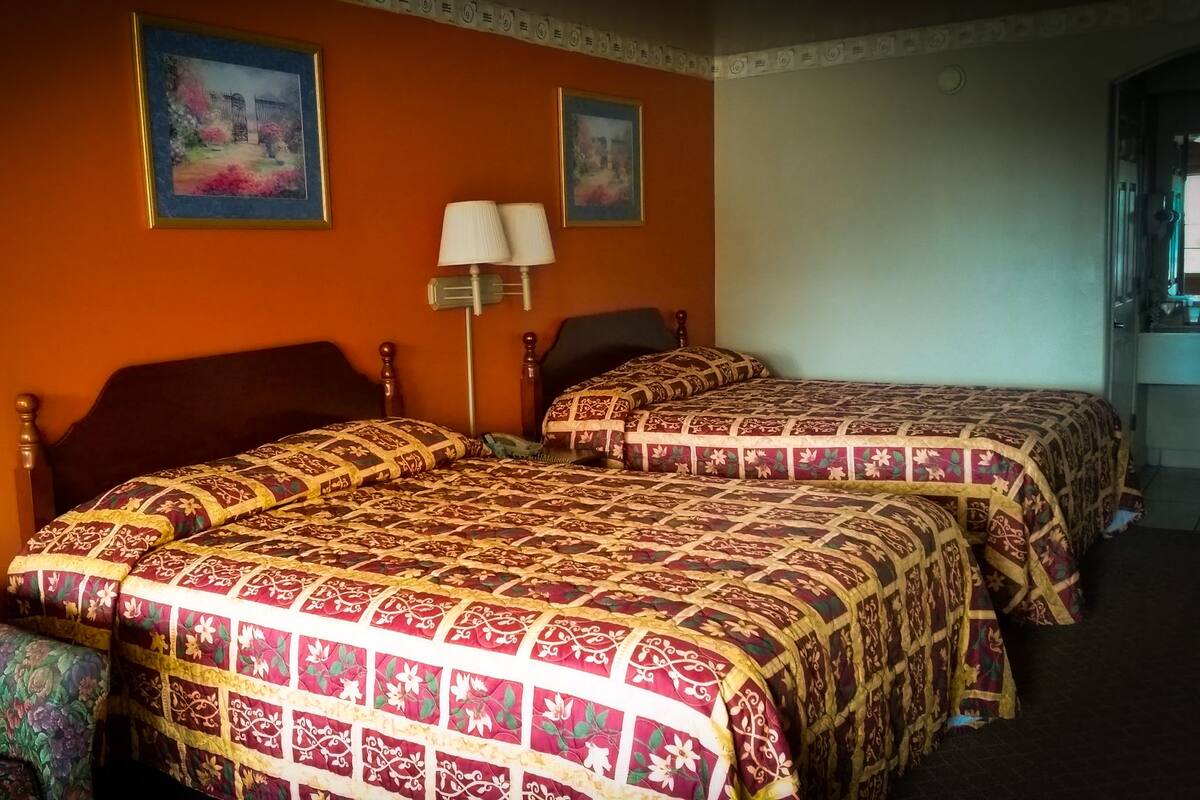A hotel room with two beds, a chair, and two wall-mounted lamps.