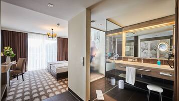 Hotelkamer met een bed, een bureau met stoel, een grote spiegel, een badkamer met wastafel en toilet, en een raam met gordijnen.