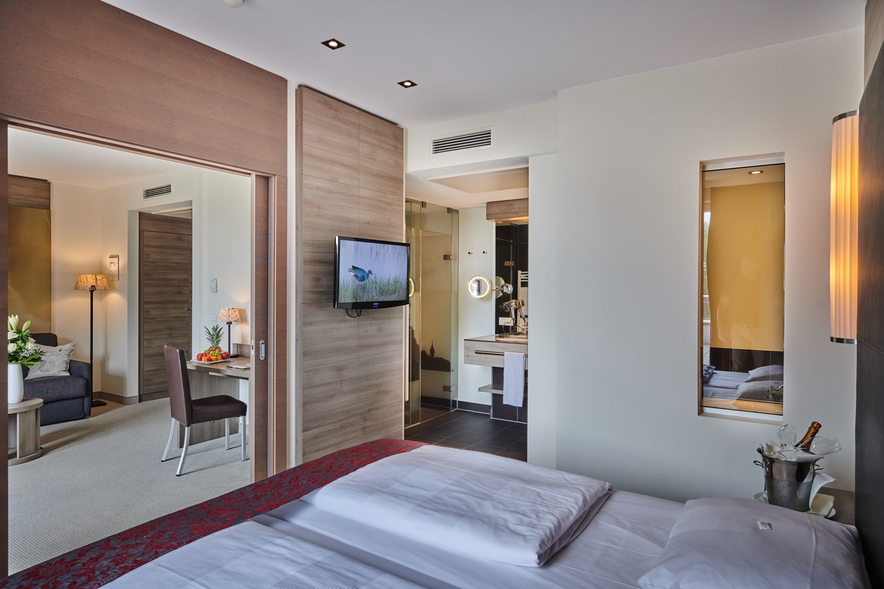 Una moderna camera d'albergo con un letto grande, una scrivania con una sedia, una televisione, uno specchio e un frigobar.
