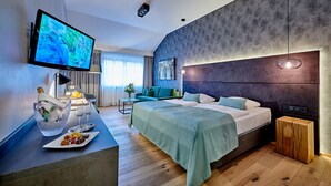 A modern hotel room with a large bed, a flat-screen TV, a small seating area with a table and chairs, and a decorative plant.
