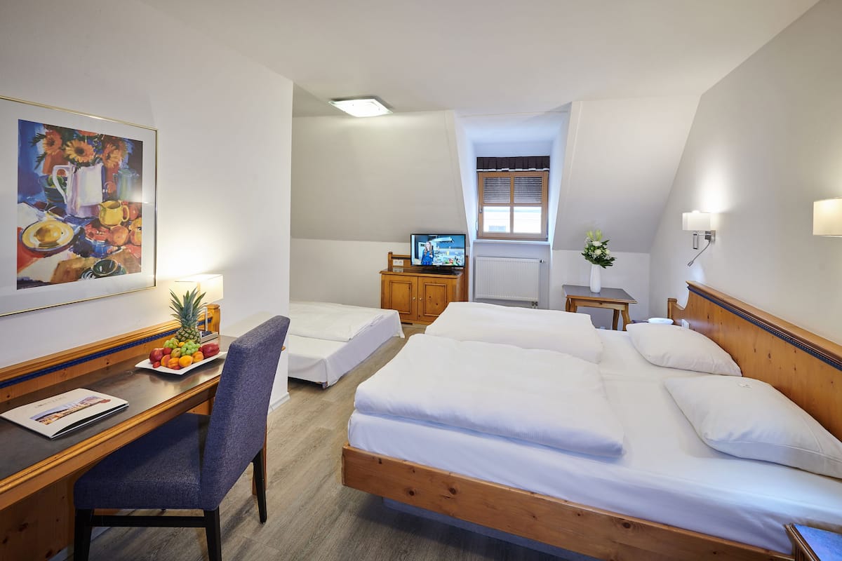A hotel room with a wooden bed, a desk with a chair, a television, a framed painting, and a window with blinds.