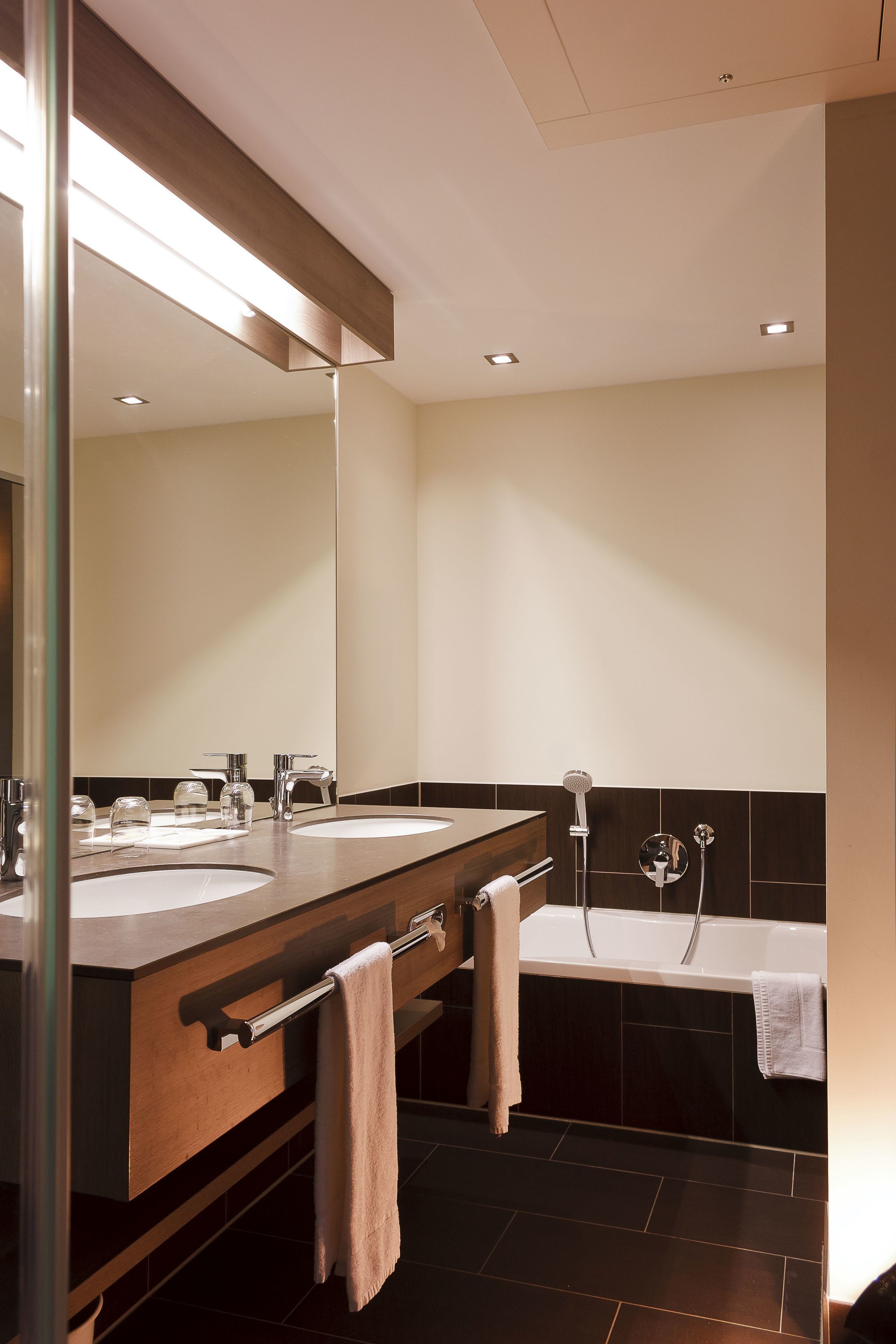 A modern bathroom with two sinks, a large mirror, a bathtub, and a towel rack.