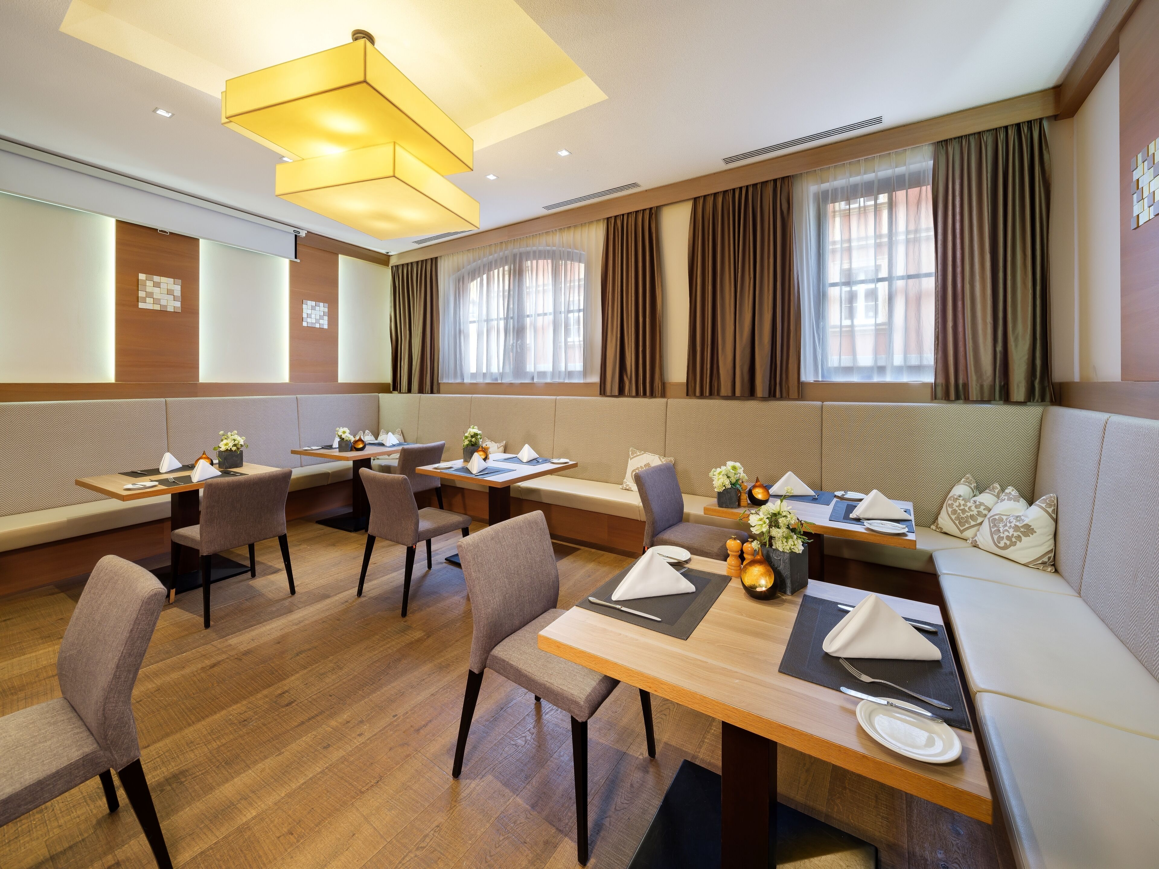 A modern dining area with booths and tables, wooden flooring, and large windows with curtains.