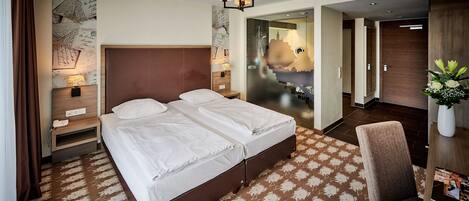 A hotel room with a large bed, a bedside table with a lamp, a chair, and a desk with a vase of flowers.