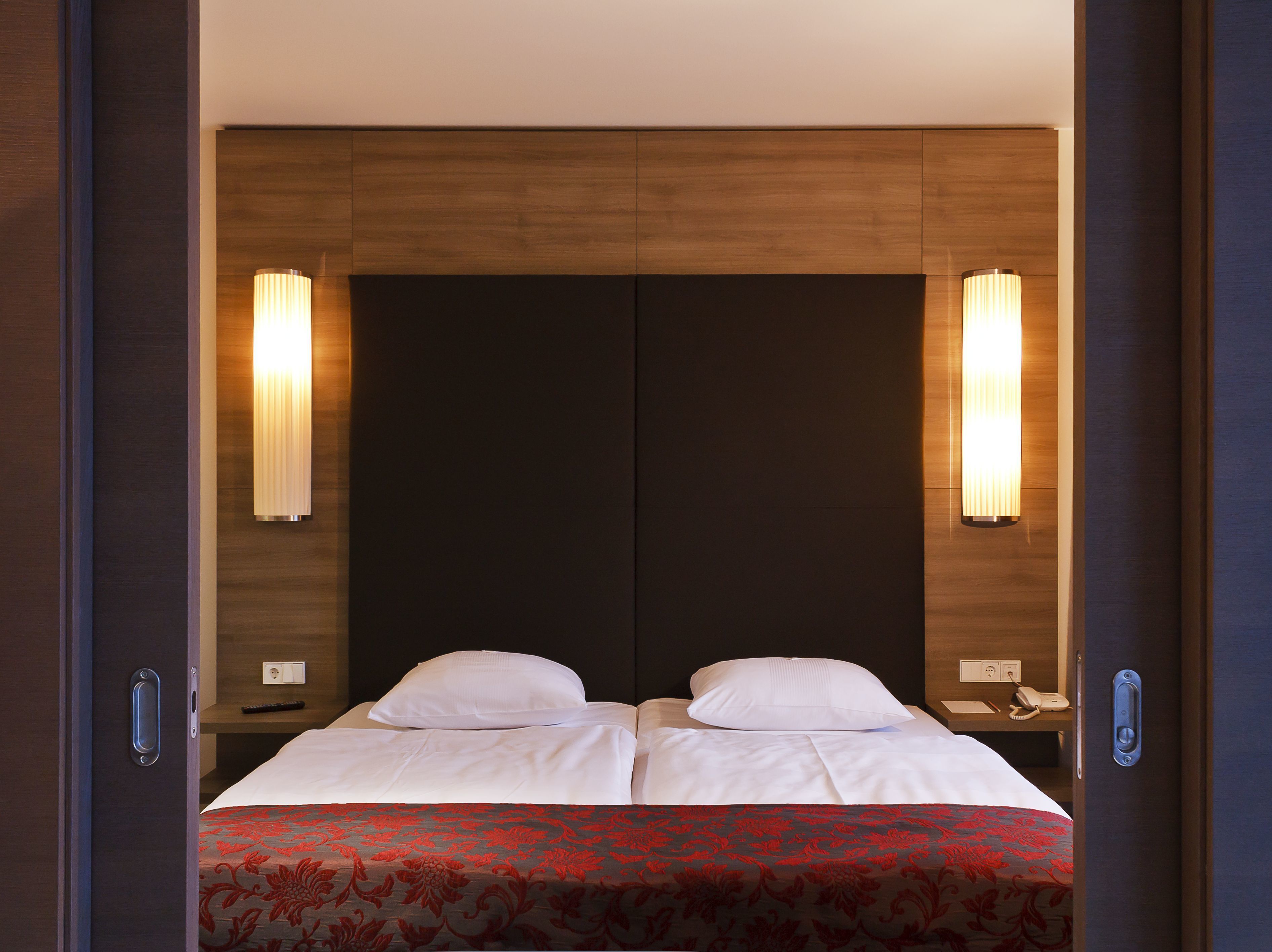 A double bed with a red and black patterned bedspread, two bedside tables with lamps, and a dark wooden headboard.