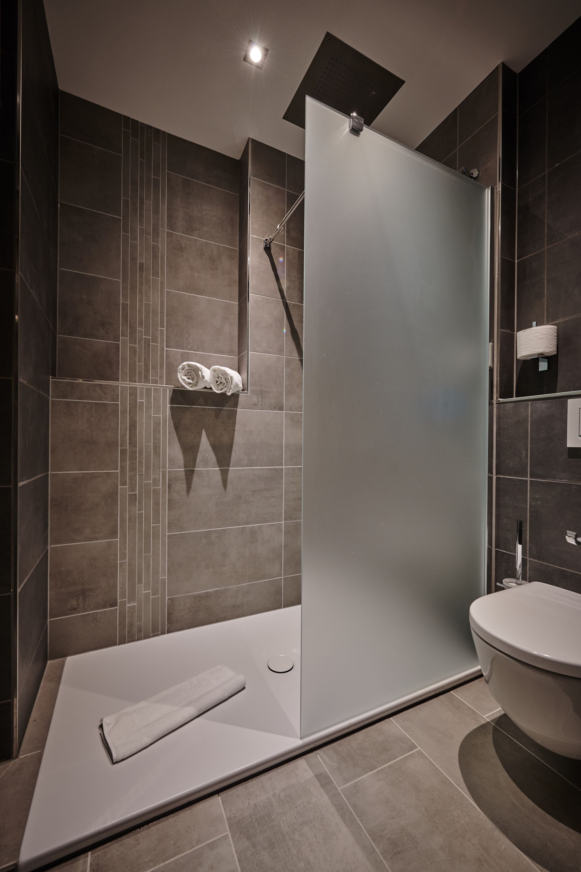 Un baño moderno con ducha envuelta en vidrio, un inodoro y un perchero con toallas.