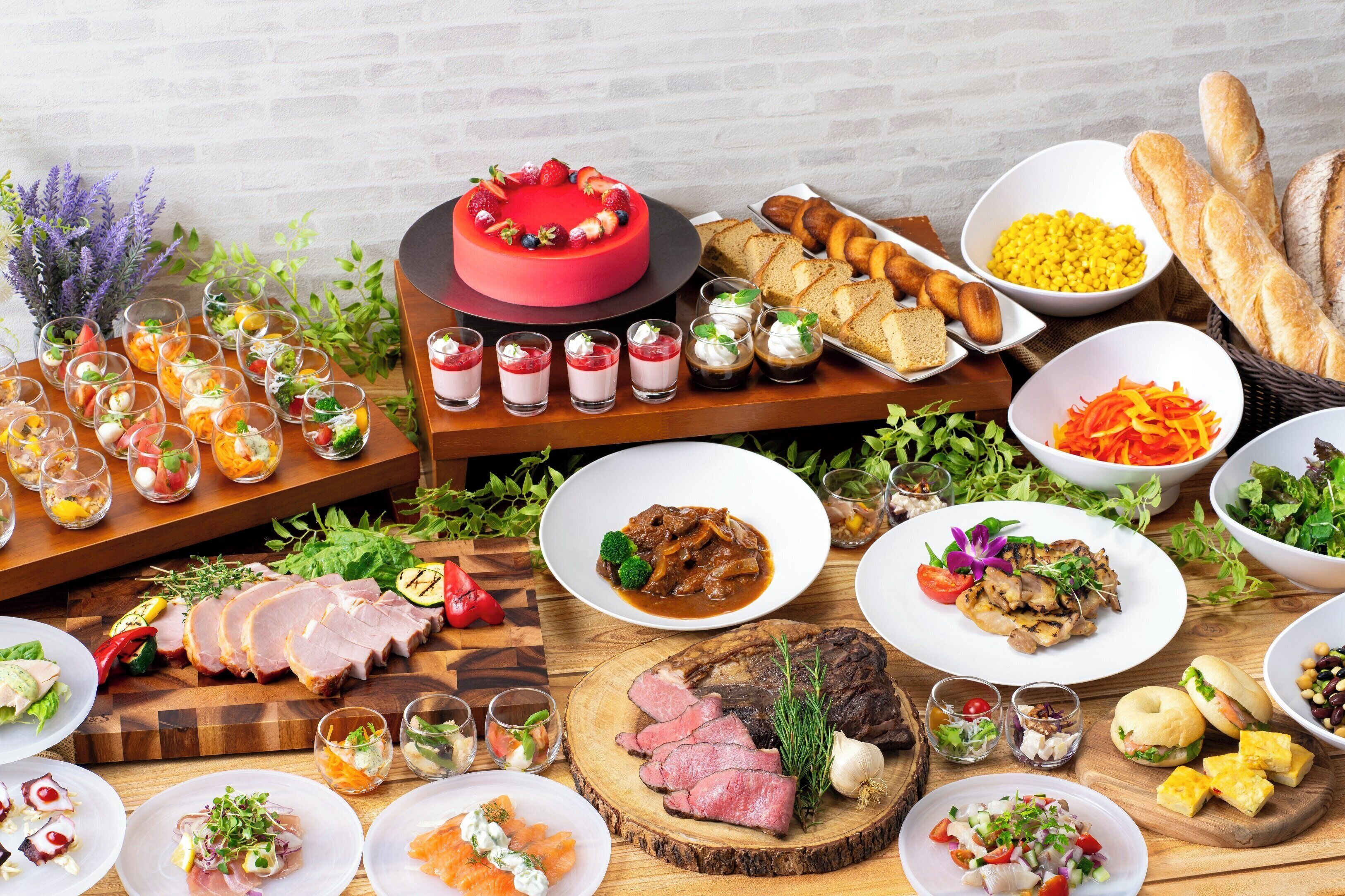 A variety of food items including a red cake, sliced meats, and various salads on a wooden table.