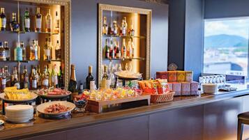 A bar area with shelves of liquor bottles, a variety of snacks, and a view of the city through a large window.