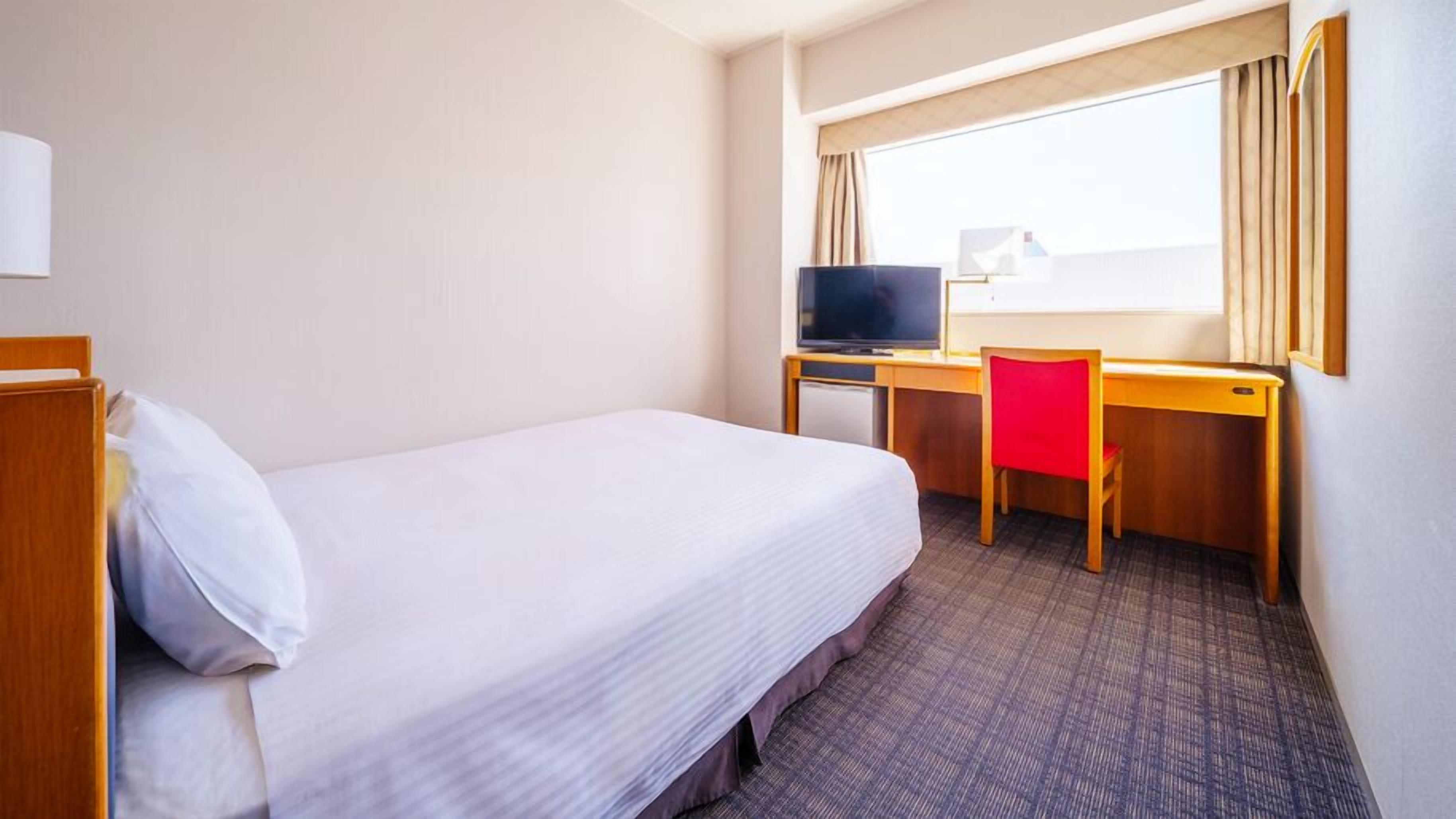 A hotel room with a single bed, a desk with a computer, and a window with curtains.