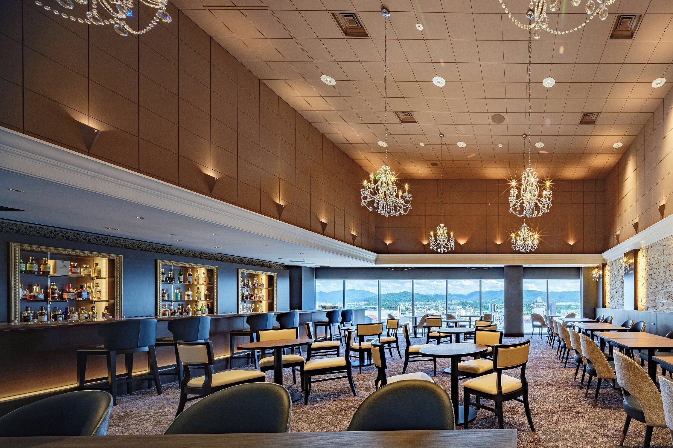 A spacious restaurant with high ceilings, chandeliers, and a bar area with shelves of bottles.