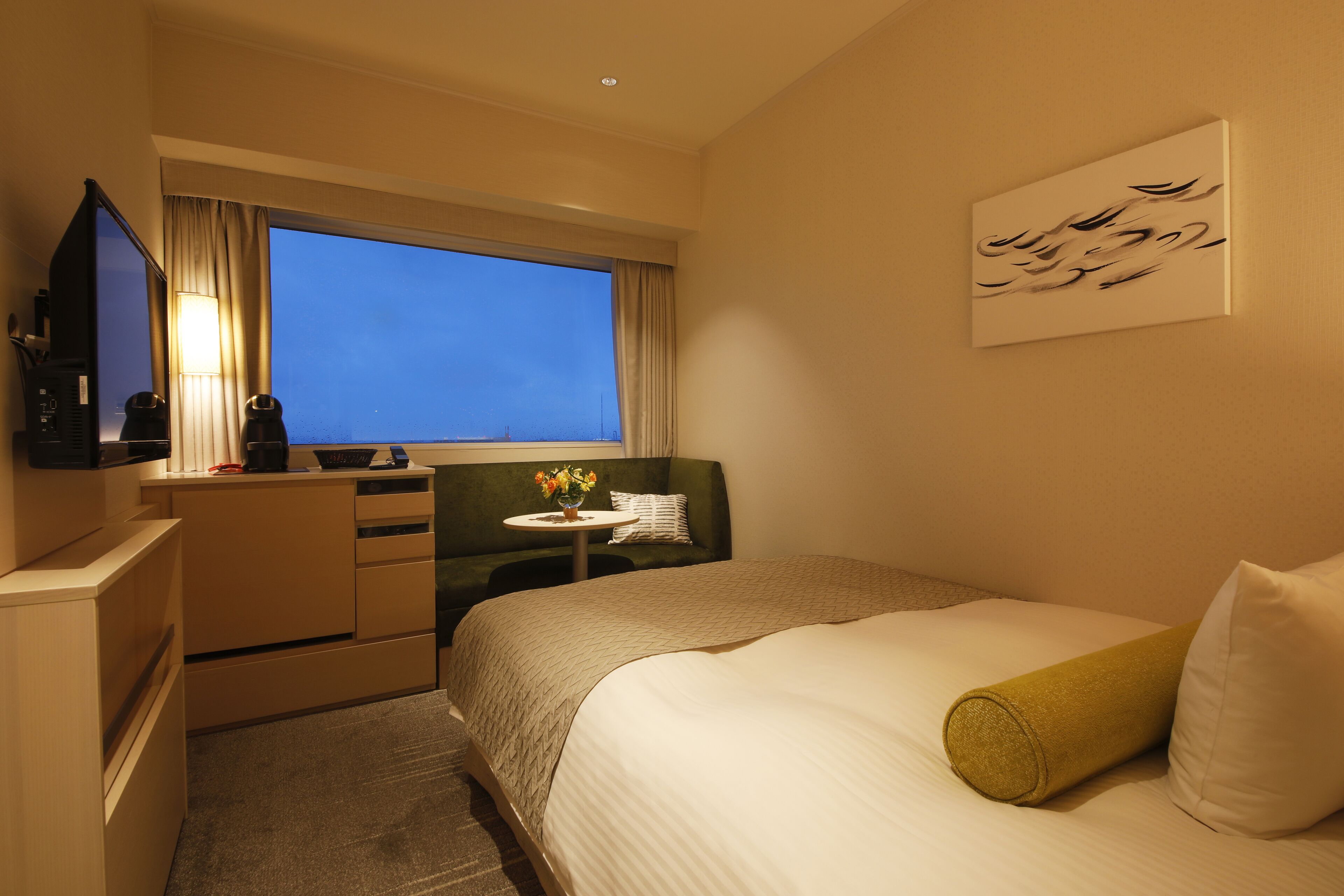 A hotel room with a bed, a desk, a television, and a window with curtains.