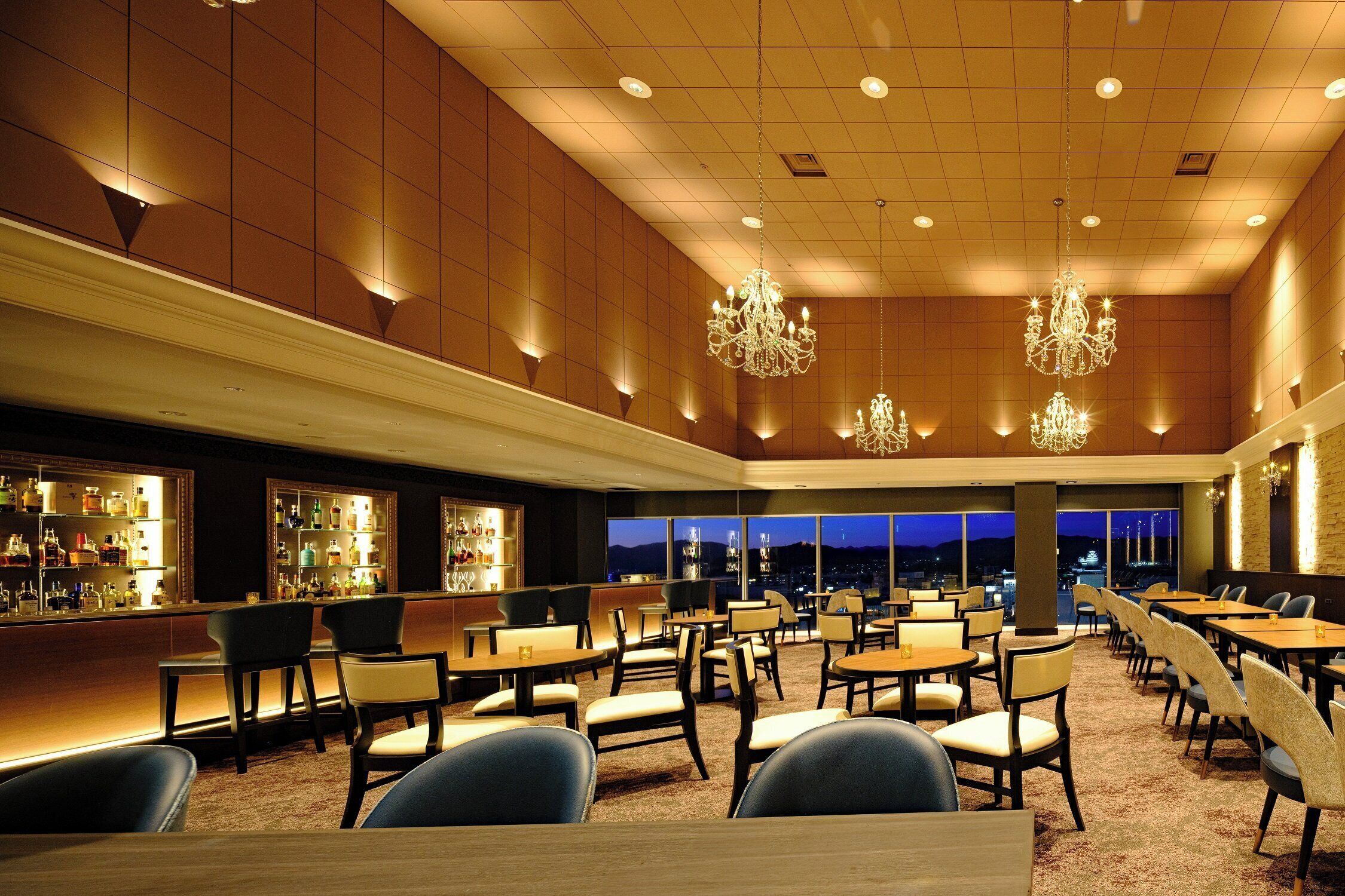 En rummelig hotellobby med barområde, flere siddepladser og store vinduer med udsigt over byen.