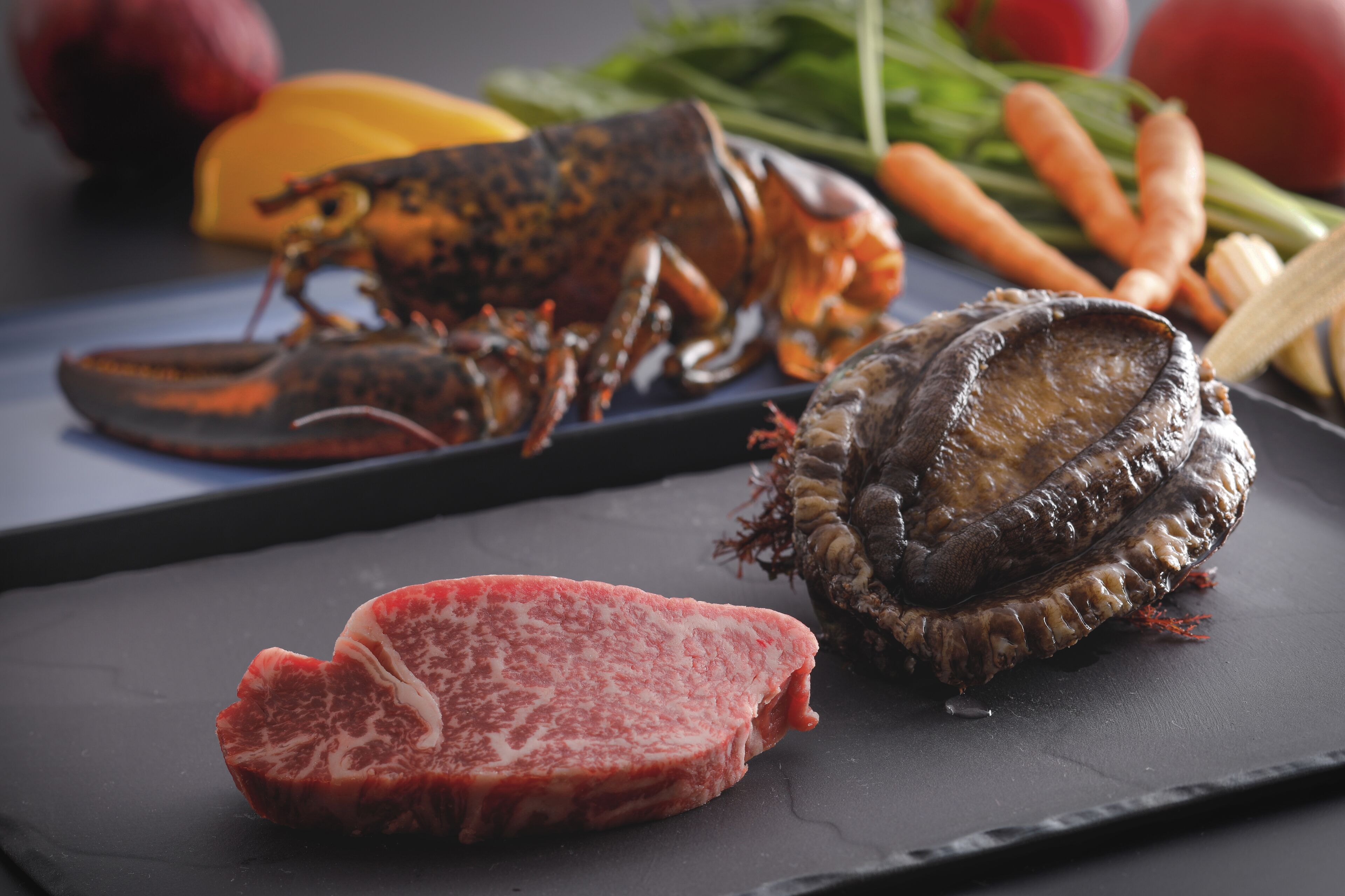 Un langostino, un trozo de carne y algunas verduras sobre una superficie oscura.