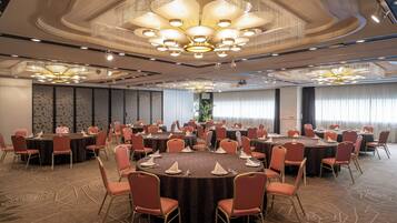 A large conference room with multiple round tables, each surrounded by chairs, and a sophisticated chandelier.