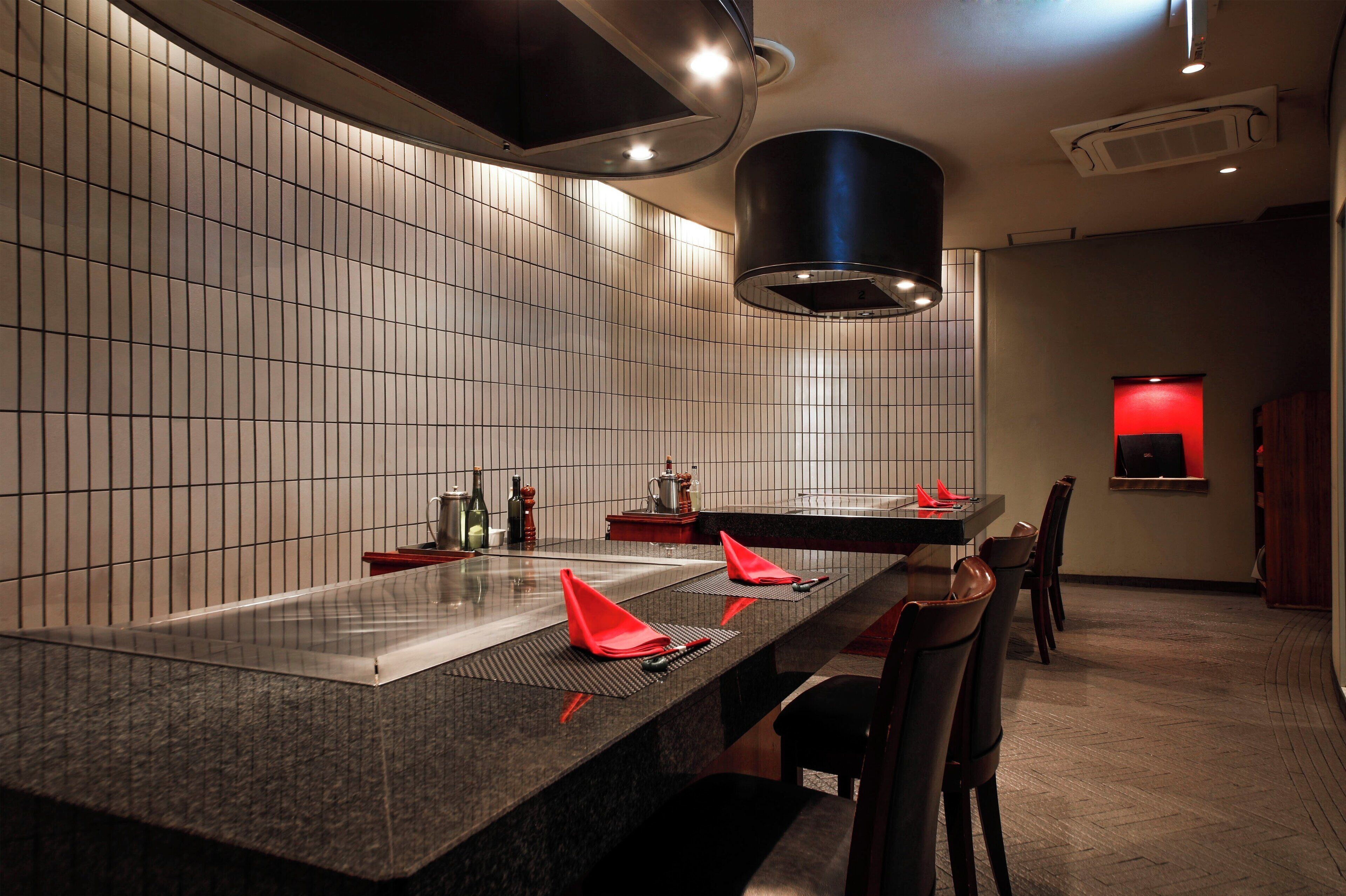A modern restaurant with a long counter, tiled walls, and a black ceiling vent.