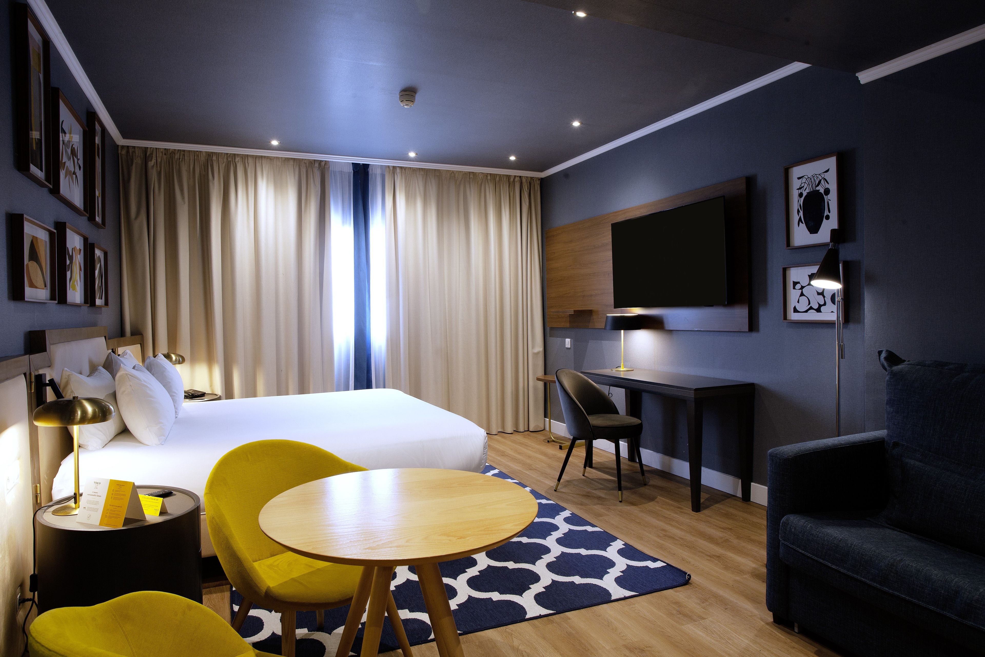Hotellihuone, jossa on sänky, työpöytä, tuoli, sohva ja televisio.