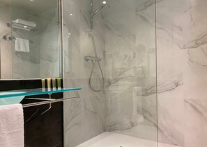 A modern bathroom with a glass shower enclosure, marble walls, and a glass countertop with toiletries. - voco Madrid - Las Tablas by IHG (Madrid)