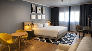 A hotel room with a bed, a desk, a chair, a sofa, and artwork on the wall. - voco Madrid - Las Tablas by IHG (Madrid)