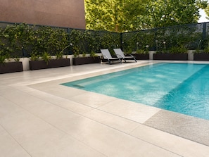Piscina con suelo de baldosas y dos sillas de descanso.