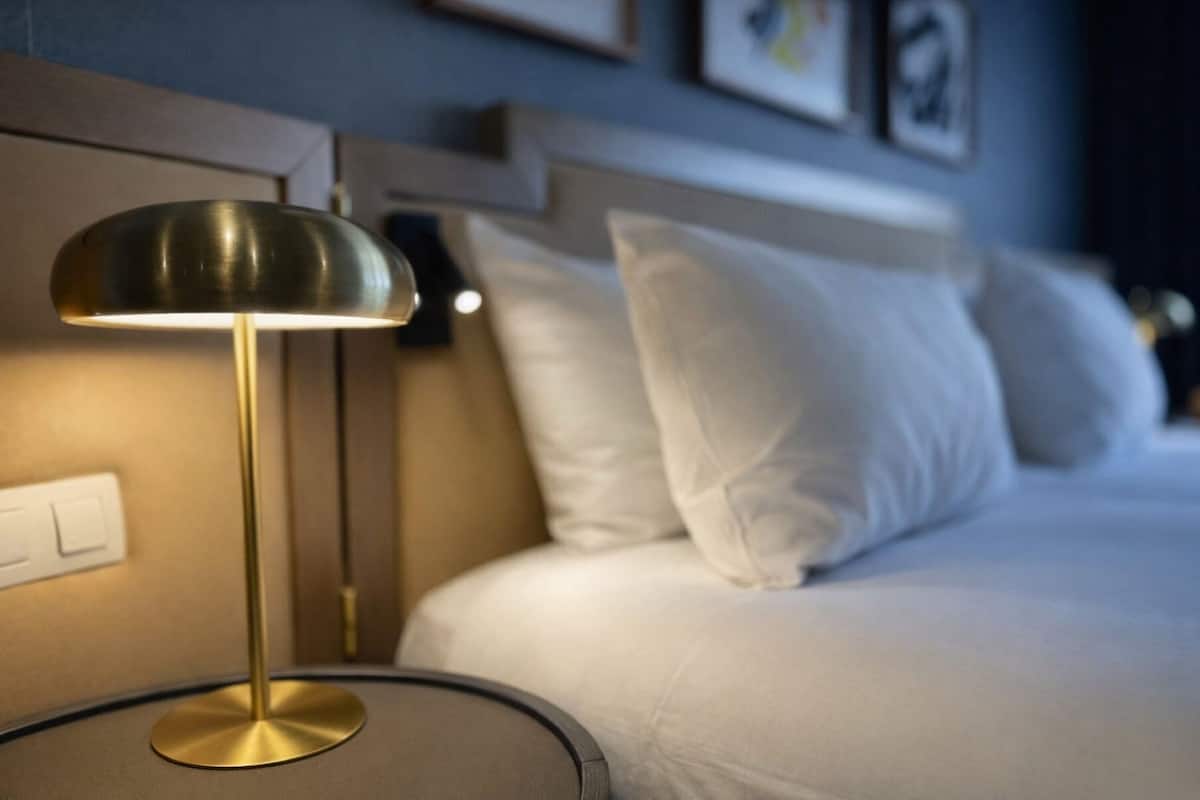 Ein Bett mit weißer Bettwäsche, eine Nachttischlampe und ein an der Wand montierter Lichtschalter.