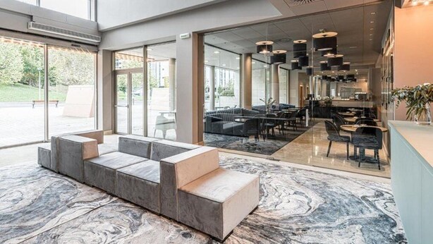 Un lobby moderno con zona de estar, mostrador de recepción y comedor con mesas y sillas.