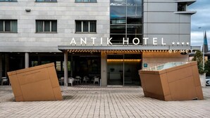 Exterior del Hotel Antik, con fachada moderna, amplios ventanales de vidrio y una entrada destacada.