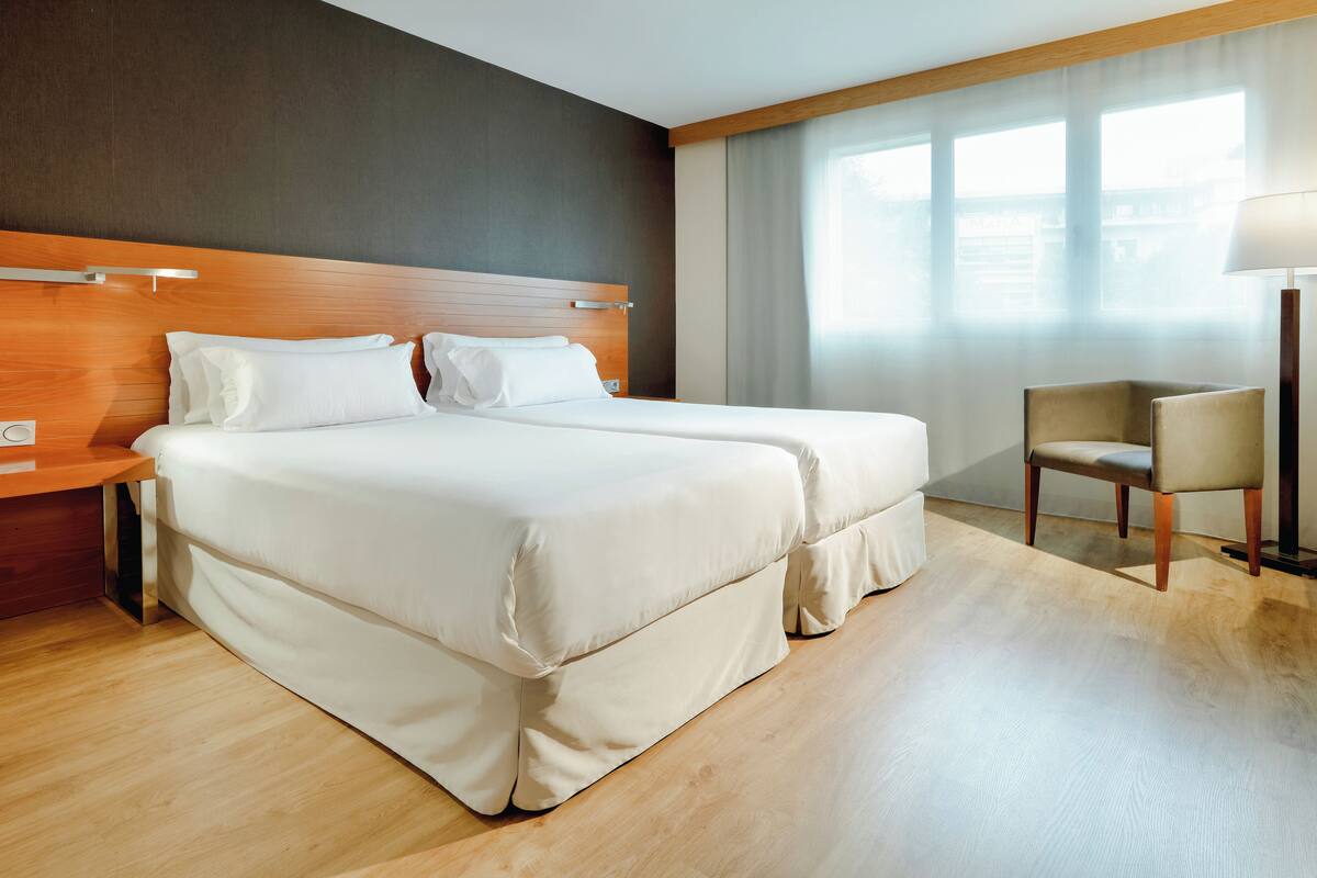 A hotel room with a double bed, a wooden headboard, a chair, and a lamp.