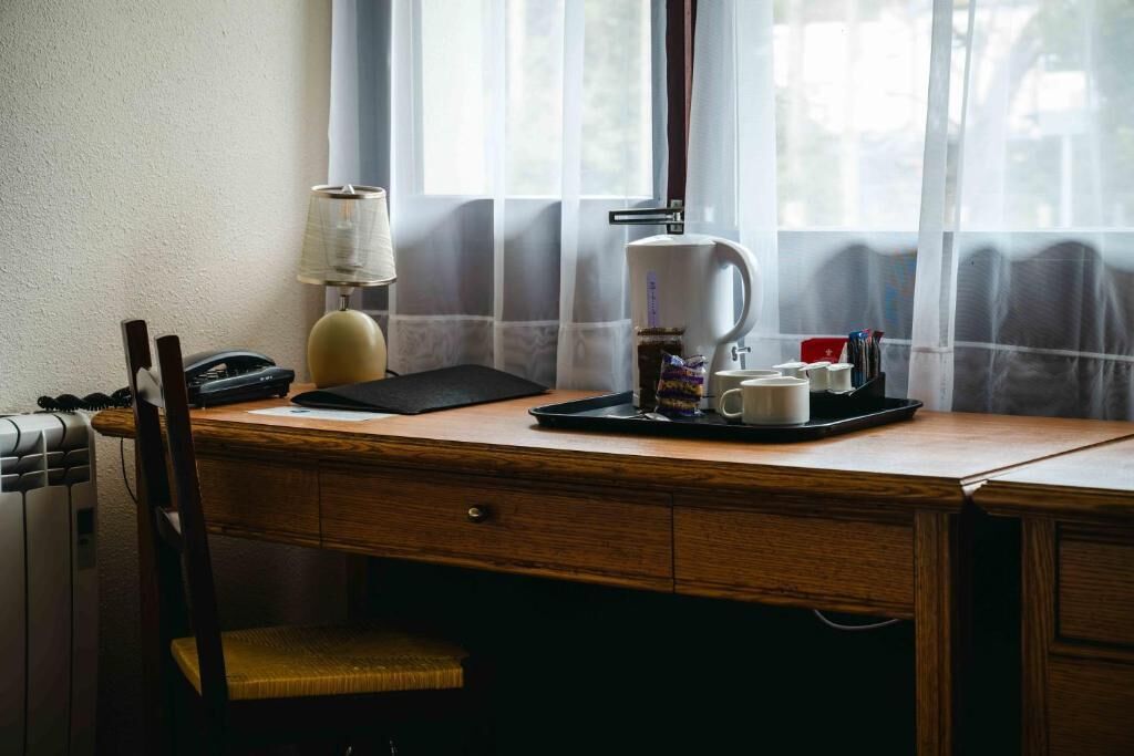 A wooden desk with a lamp, a coffee maker, and a tray with cups and a phone.