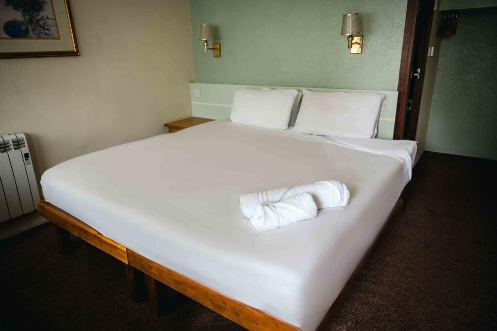 Ein Hotelzimmer mit einem großen Bett, zwei Nachttischlampen, einem gerahmten Bild an der Wand und einer Heizung.