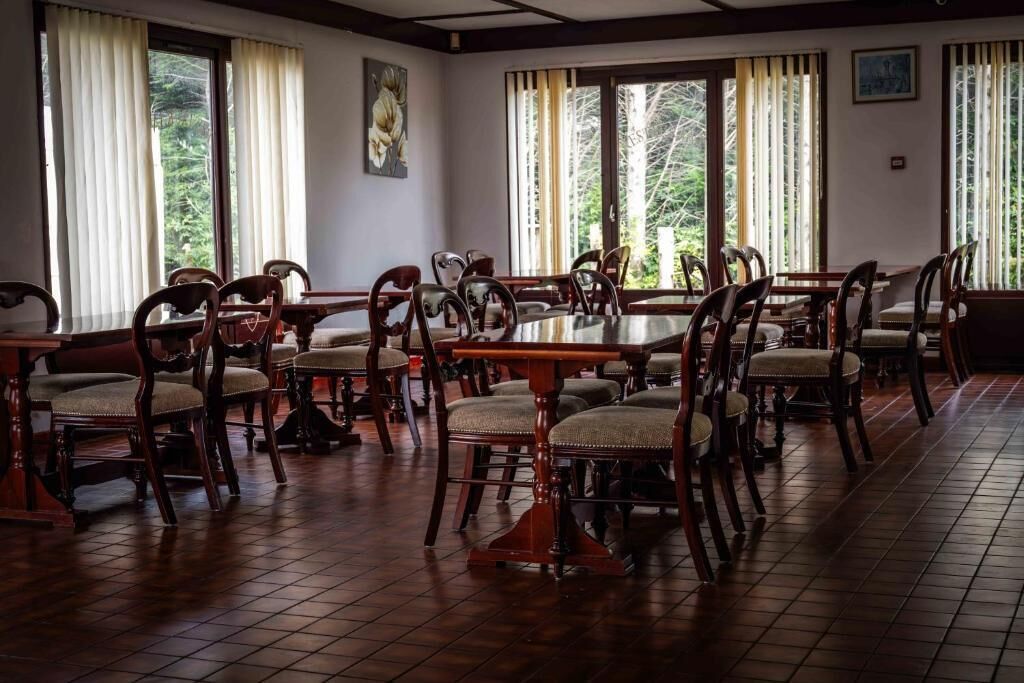Un comedor con mesas y sillas de madera, ventanas amplias con cortinas y obras de arte en las paredes.