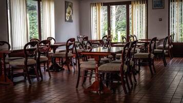 Un comedor con mesas y sillas de madera, ventanas amplias con cortinas y obras de arte en las paredes.