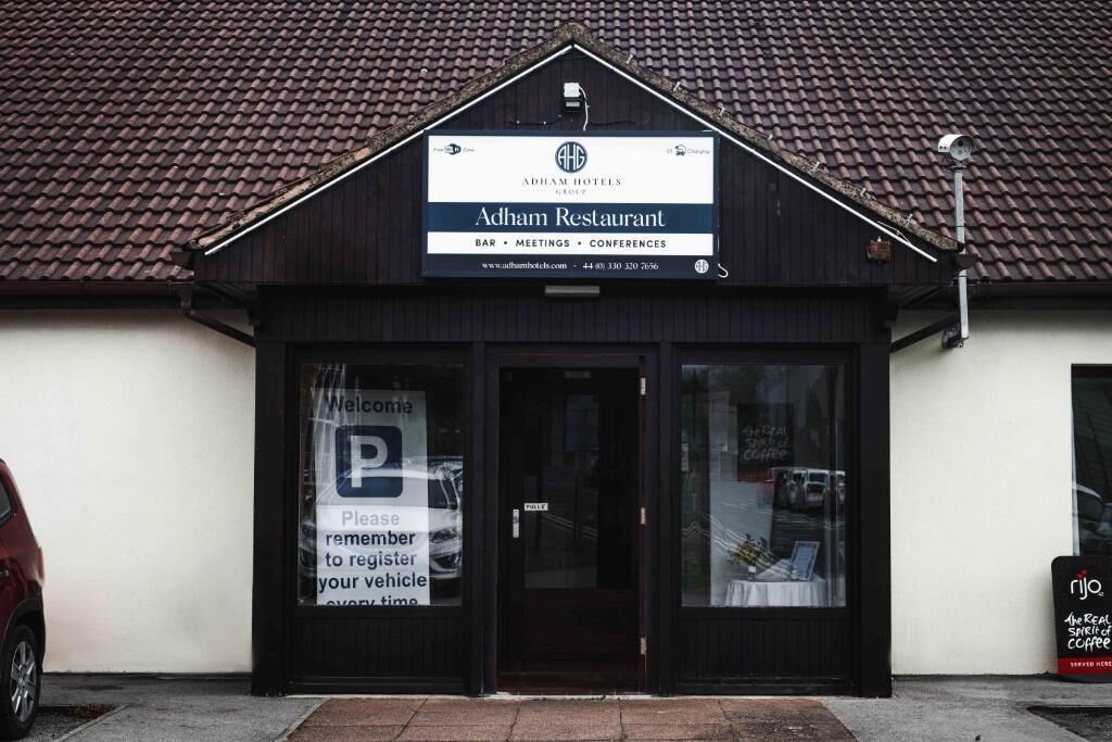 Restaurant Adham mit einem Schild, das Dienstleistungen wie Bar, Tagungen und Konferenzen anzeigt. Vor der Tür befindet sich ein Parkplatzschild und ein kleines Schild für Rijo Kaffee.