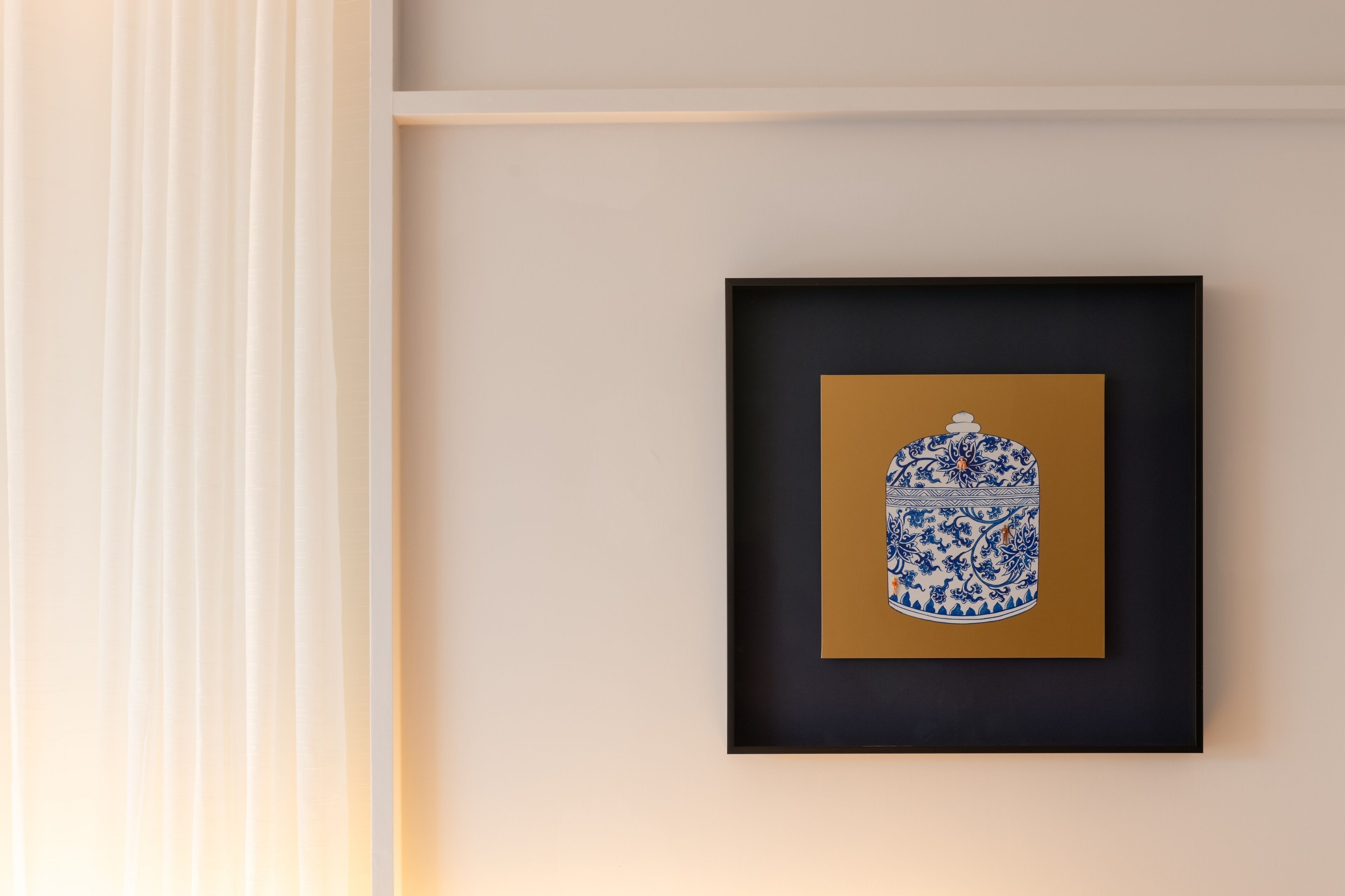 A framed artwork of a blue and white ceramic pot on a wall.