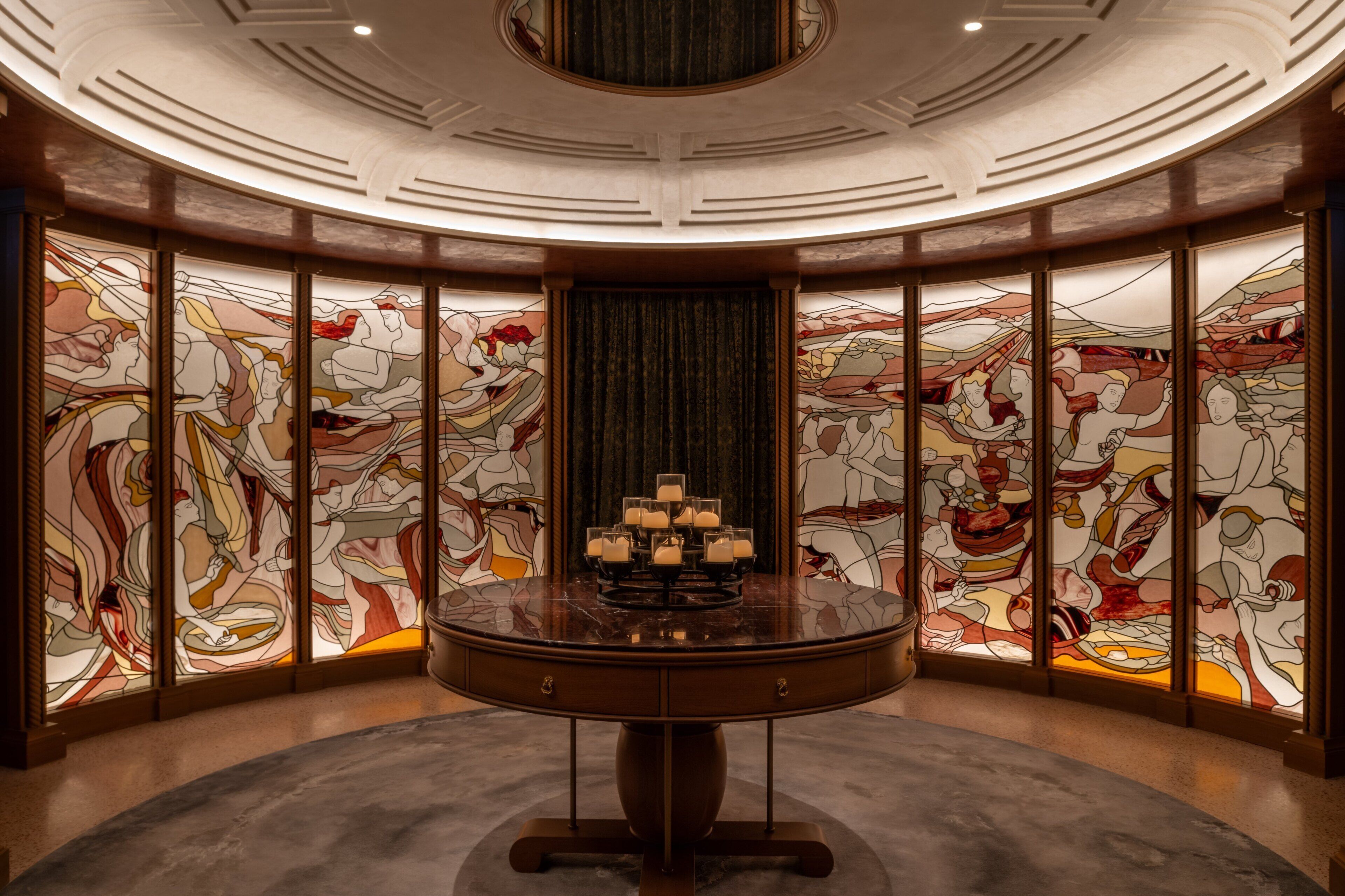 A round table with candles in the center, surrounded by stained glass panels with abstract designs.